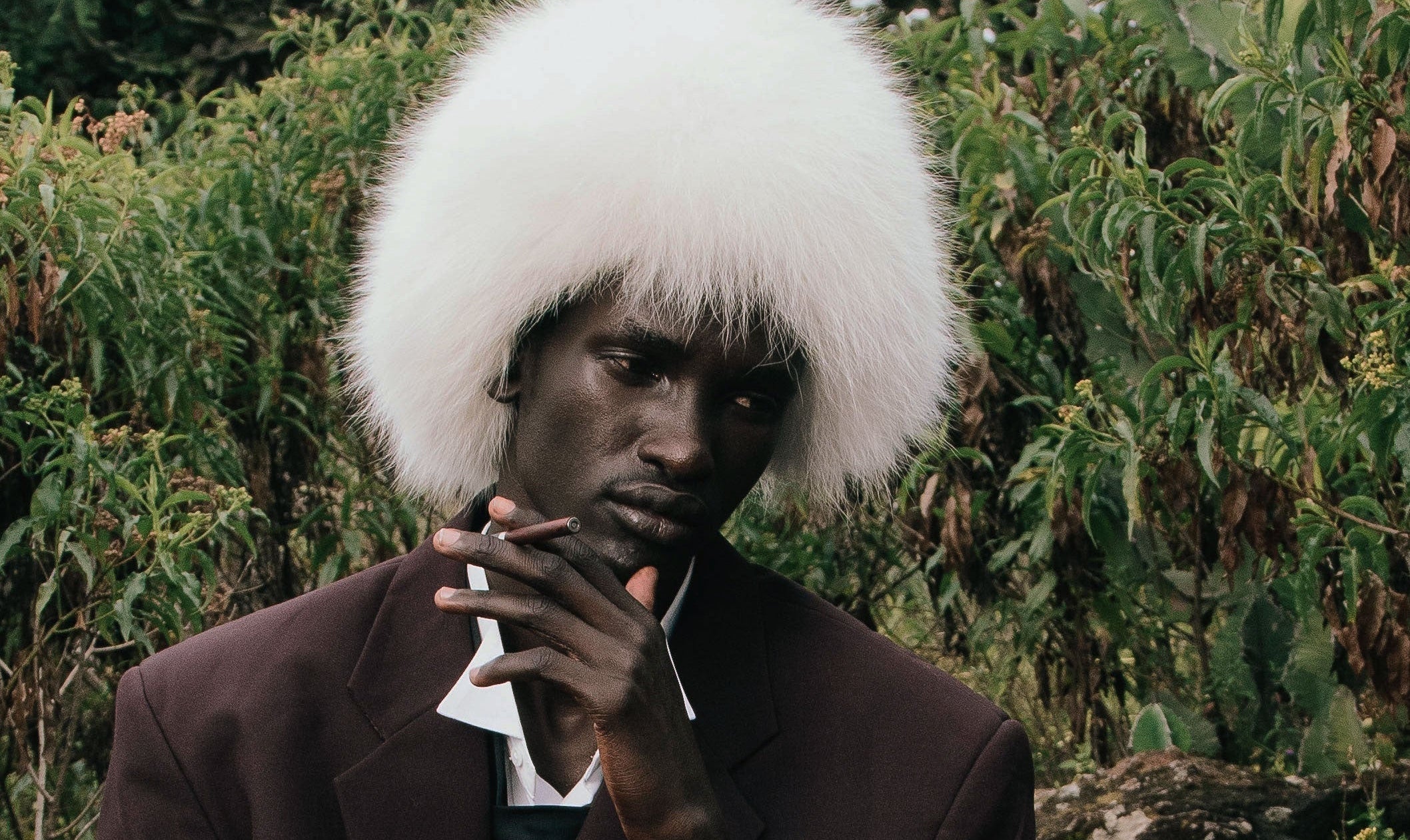 Person with white fur hat and dark clothing against a green foliage background